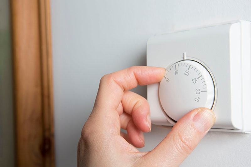 A person's hand adjusting a thermostat