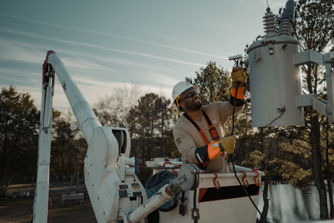 An Alabama Power lineman in a bucket truck smiles as he repairs a transformer.