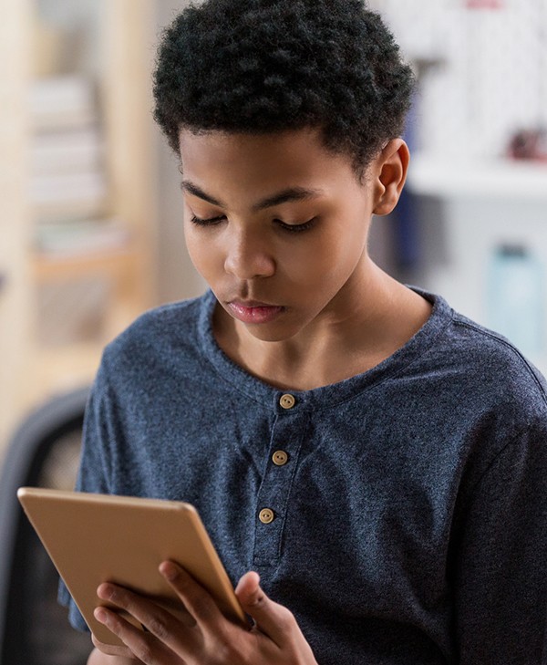 African American teenage boy has a serious expression on his face as he uses a digital tablet to research a topic for a paper.