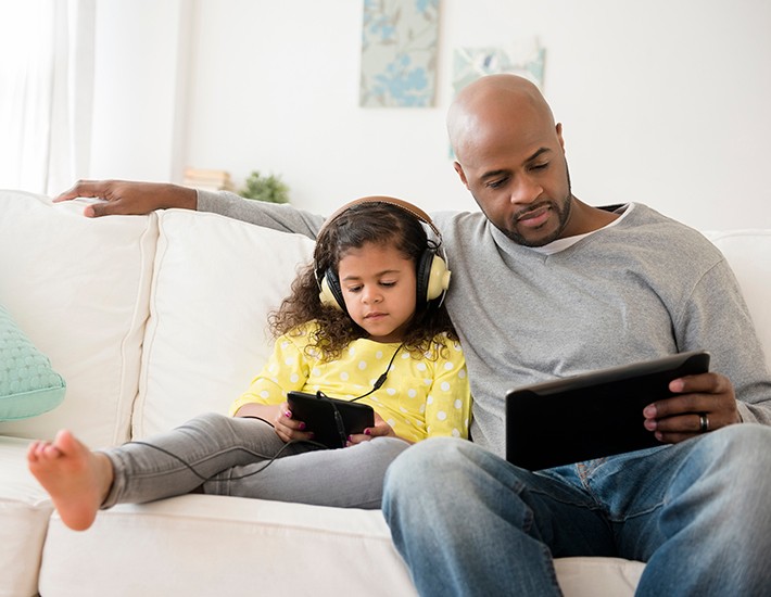 Father and daughter using digital tablets on sofa
