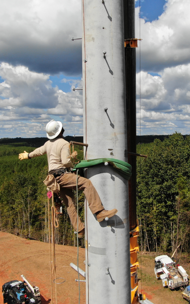 An Alabama Power Lineman high up on a transmission pole directs a crane operator during construction.