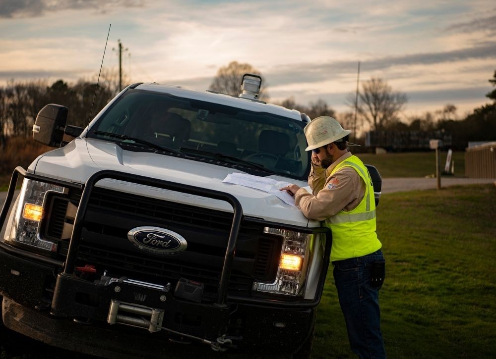 ground crew member leaning on fleet truck while talking on the phone