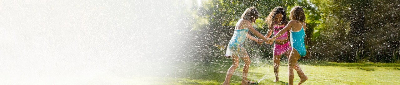 Three girls play in a sprinkler on a warm summer day.