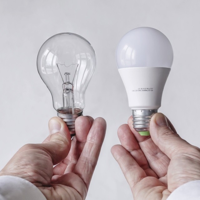 One hand holding an incandescent lightbulb and the other holding a LED lightbulb