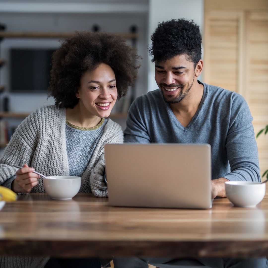 Pareja sentada en la mesa revisando una pantalla de computadora portátil juntos