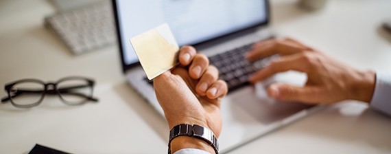 Person reviewing information on a post-it note while on their laptop 