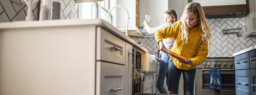 Tween girls doing dishes in modern kitchen