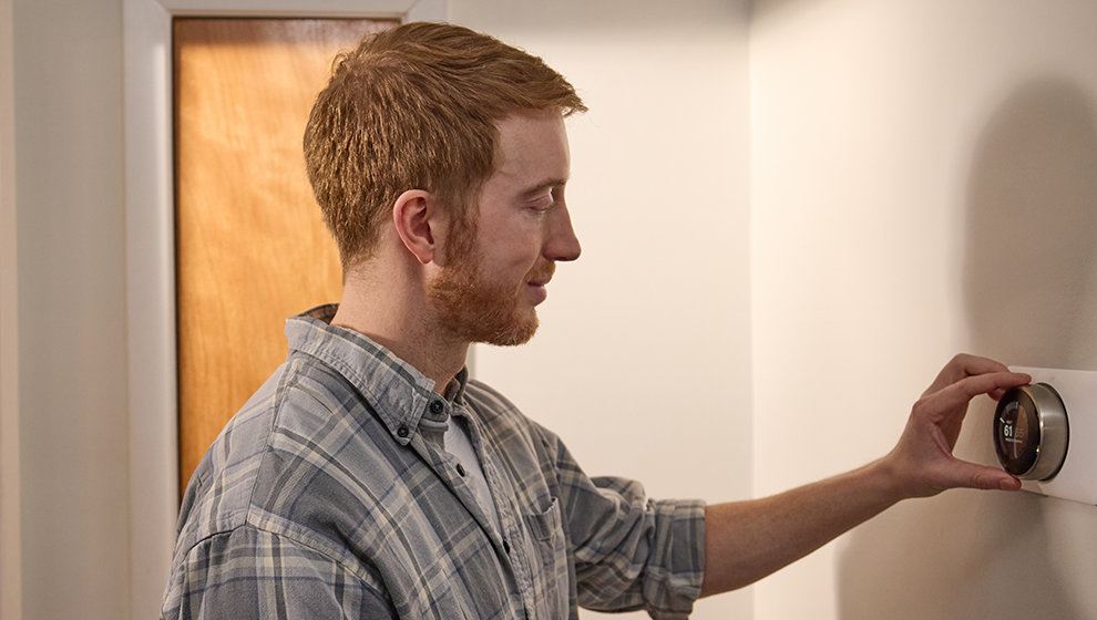 A man adjusts his thermostat for optimal cost savings on energy.